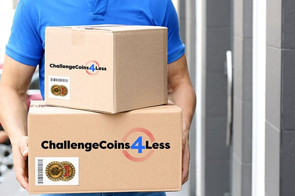 A delivery person in a blue shirt holds two cardboard boxes labeled 'ChallengeCoins4Less,' with visible coin design stickers, symbolizing the shipment of custom coins to a customer.