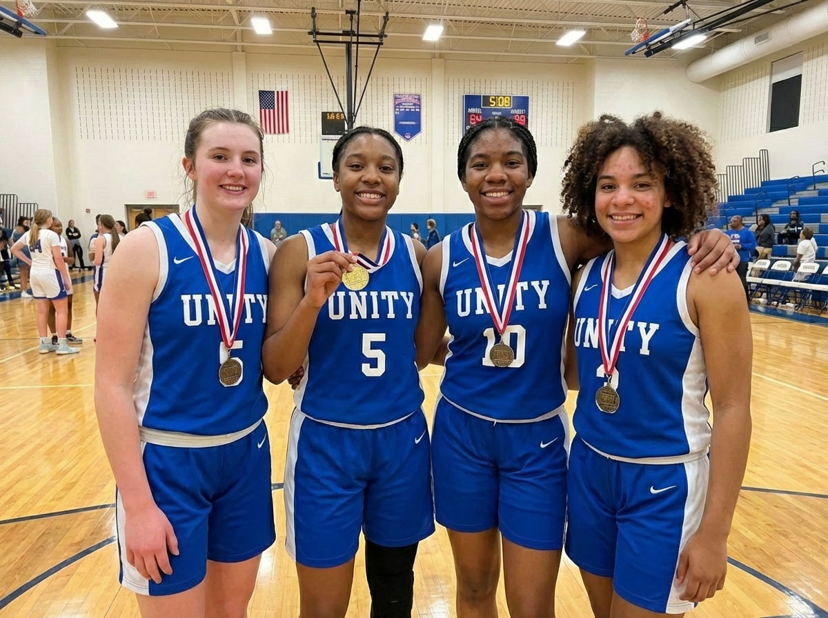Four Unity basketball players posing together on the court wearing gold medals around their necks.