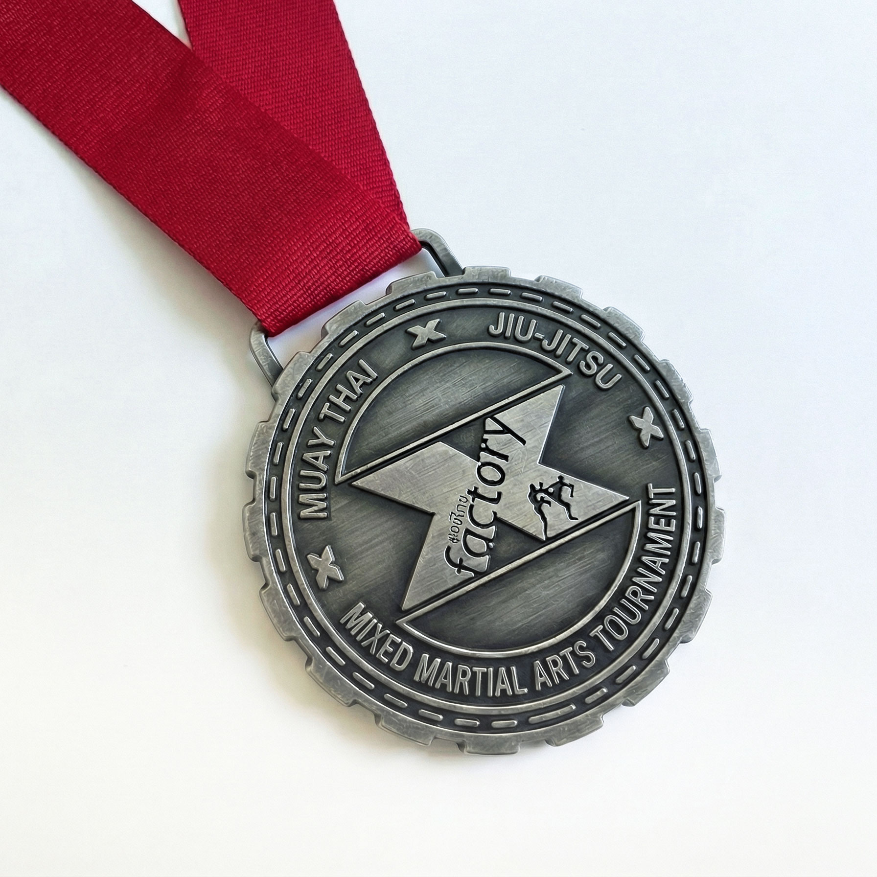 Antique silver X Factory Muay Thai, Jiu-Jitsu, and Mixed Martial Arts Tournament medal with fighter silhouettes and red ribbon